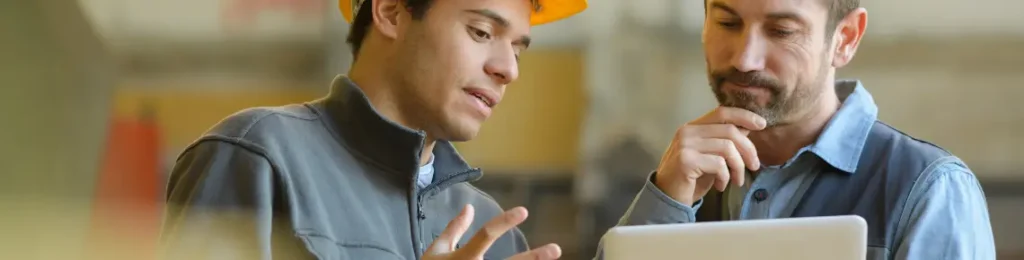 two men in hard hats talking and looking at a tablet