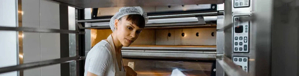 professional baker taking bread out of a commercial oven